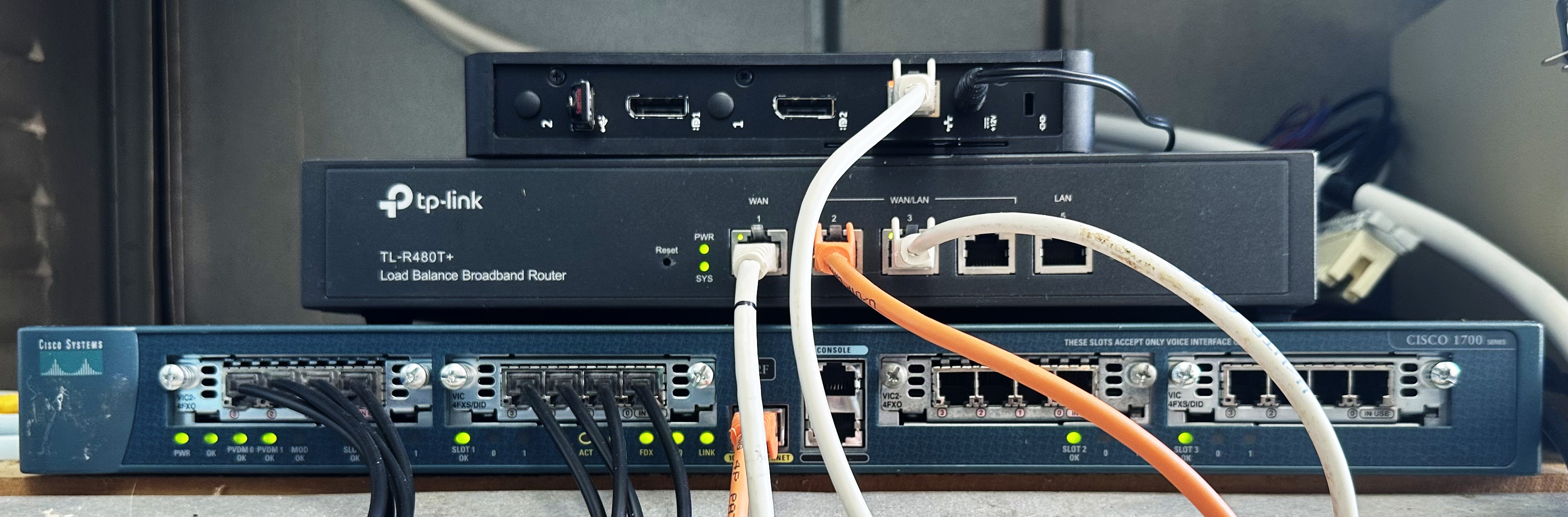 photo of a small stack of networking equipment, with a cisco 1760, a TP-Link TL-R480T and a Dell thin client